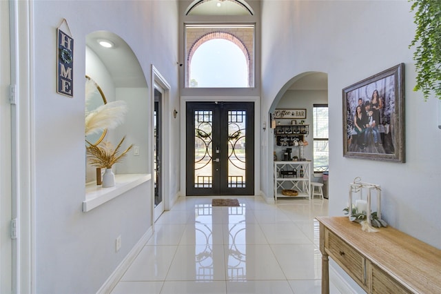 entryway with light tile patterned floors, baseboards, arched walkways, a high ceiling, and french doors