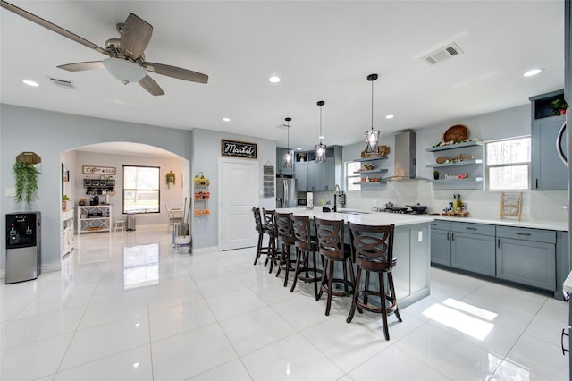 kitchen with arched walkways, visible vents, wall chimney exhaust hood, and open shelves