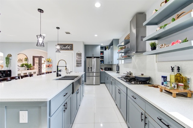 kitchen with arched walkways, stainless steel appliances, wall chimney range hood, open shelves, and a sink