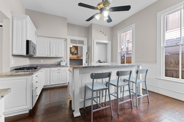 kitchen with white cabinets, a center island with sink, appliances with stainless steel finishes, and dark wood finished floors