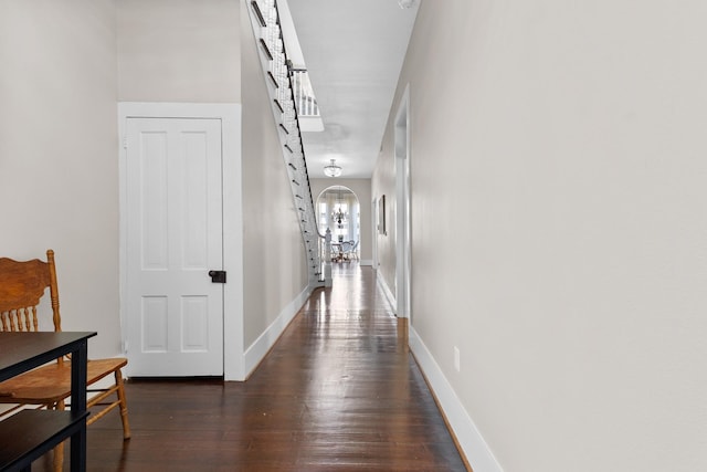 hallway featuring arched walkways, dark wood-style flooring, and baseboards