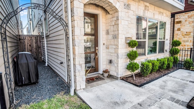 view of exterior entry featuring stone siding and fence