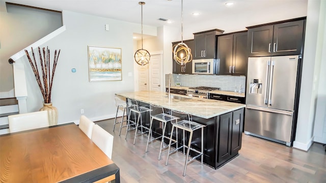 kitchen with premium appliances, a breakfast bar, light stone countertops, backsplash, and wood finished floors