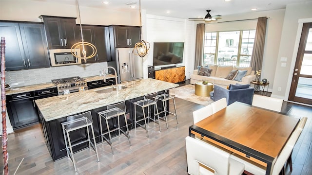 kitchen with a kitchen island with sink, a sink, a kitchen breakfast bar, decorative backsplash, and high end appliances