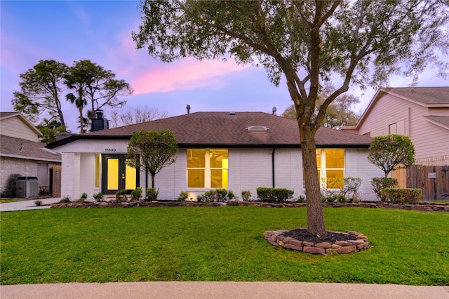 view of front of property with central AC unit, brick siding, fence, a yard, and a chimney