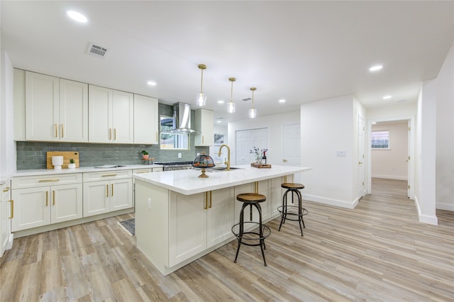 kitchen featuring tasteful backsplash, visible vents, light wood-style flooring, and wall chimney exhaust hood