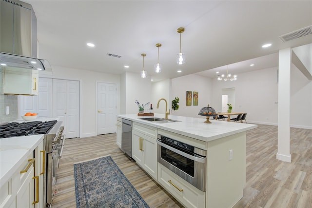 kitchen featuring appliances with stainless steel finishes, a sink, extractor fan, light wood-type flooring, and backsplash