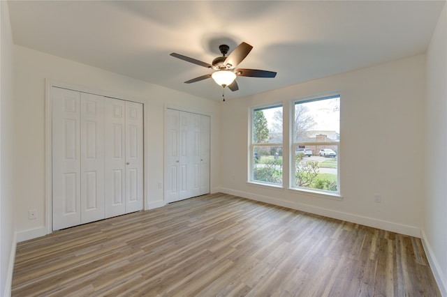 unfurnished bedroom featuring two closets, light wood-style flooring, and baseboards