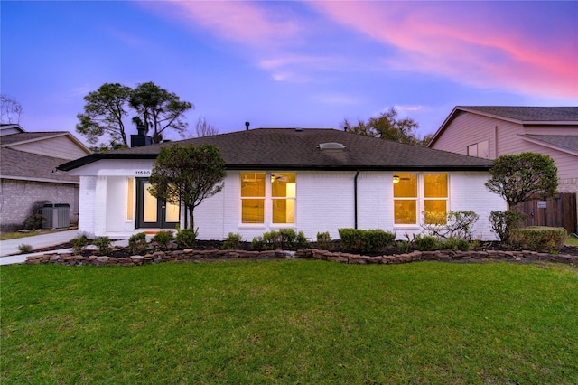 view of front of home featuring central air condition unit, roof with shingles, a front lawn, and brick siding