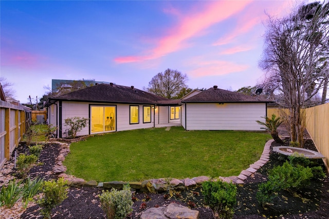 back of property at dusk with a fenced backyard and a lawn