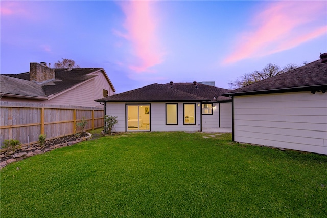 back of house at dusk with a yard and fence