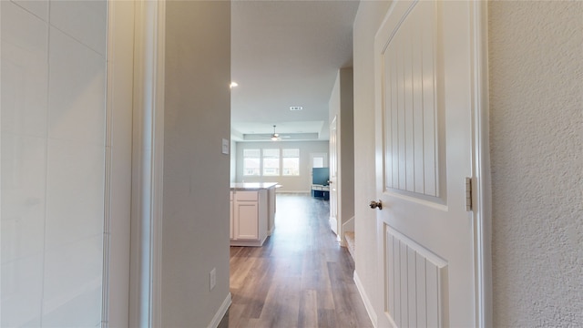 hallway with light wood-type flooring, a textured wall, and baseboards