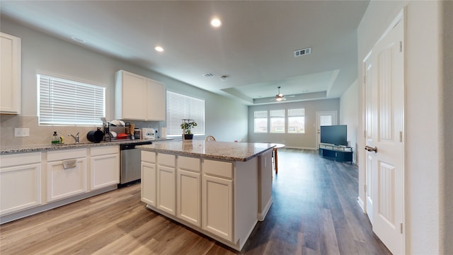 kitchen with visible vents, light wood finished floors, backsplash, dishwasher, and a tray ceiling