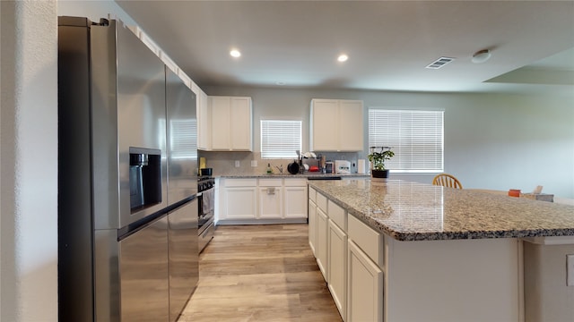 kitchen featuring stainless steel appliances, a kitchen island, visible vents, light stone countertops, and light wood finished floors