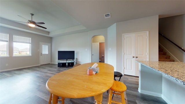 dining room featuring arched walkways, visible vents, stairway, a tray ceiling, and dark wood finished floors