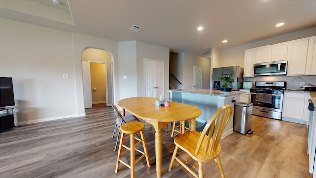 kitchen featuring light wood-style flooring, appliances with stainless steel finishes, arched walkways, and decorative backsplash