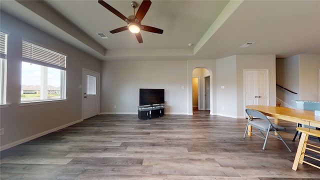 unfurnished living room featuring arched walkways, visible vents, a tray ceiling, and wood finished floors