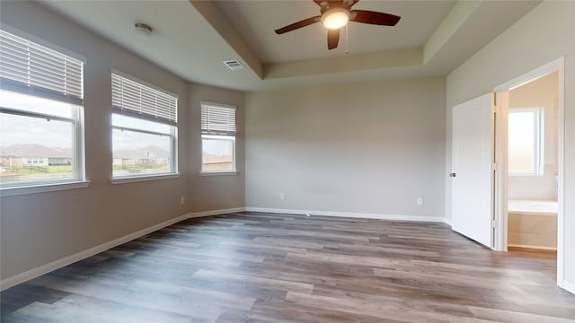 unfurnished room featuring baseboards, visible vents, a ceiling fan, wood finished floors, and a tray ceiling