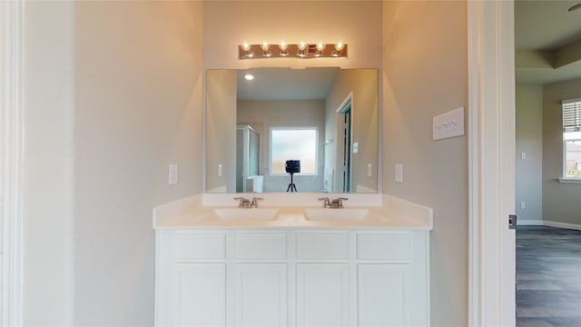 bathroom featuring double vanity, an enclosed shower, baseboards, and a sink