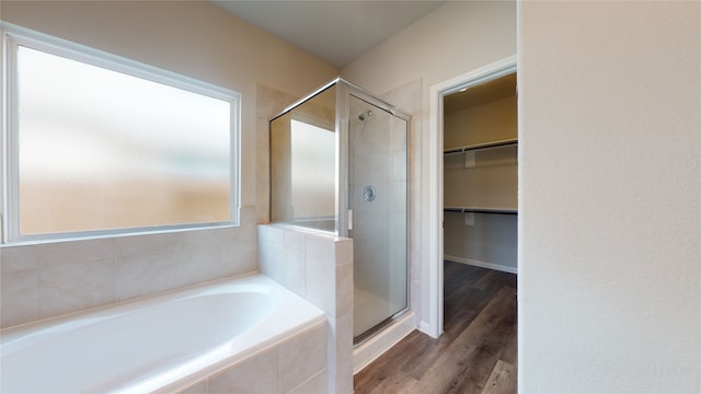 bathroom featuring wood finished floors, a garden tub, a shower stall, and a spacious closet