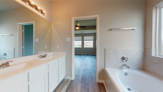 full bath featuring double vanity, wood finished floors, a sink, and a bath