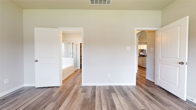 unfurnished bedroom with arched walkways, wood finished floors, visible vents, and baseboards