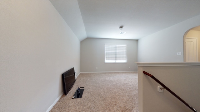 unfurnished living room with arched walkways, light colored carpet, visible vents, baseboards, and vaulted ceiling