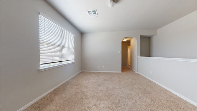 carpeted empty room with arched walkways, visible vents, and baseboards