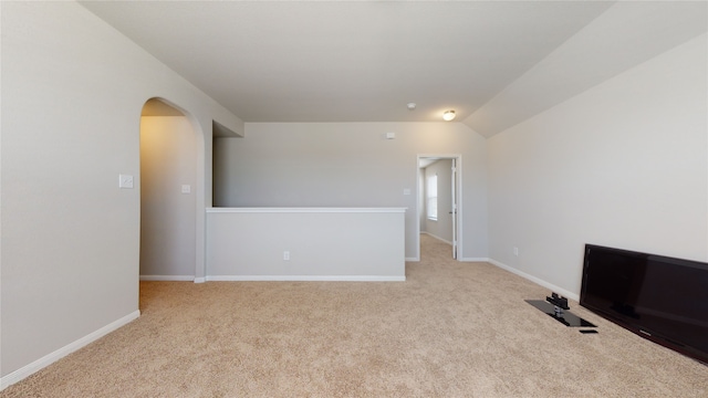 carpeted empty room with lofted ceiling, baseboards, and arched walkways