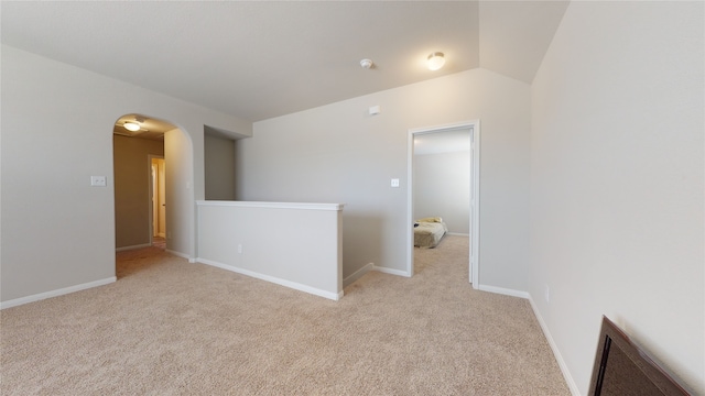 spare room featuring baseboards, arched walkways, vaulted ceiling, and light colored carpet