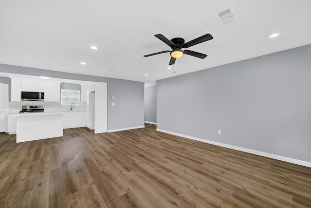 unfurnished living room with visible vents, a ceiling fan, a sink, wood finished floors, and baseboards