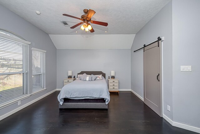 bedroom with a barn door, wood finished floors, visible vents, baseboards, and vaulted ceiling