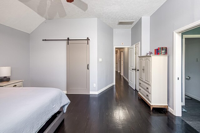 bedroom with a textured ceiling, a barn door, wood finished floors, and visible vents