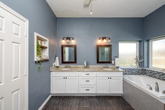 full bath with double vanity, a garden tub, a sink, and wood finished floors