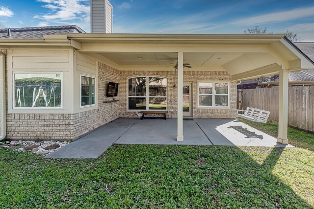 view of exterior entry featuring a yard, a patio area, fence, and brick siding