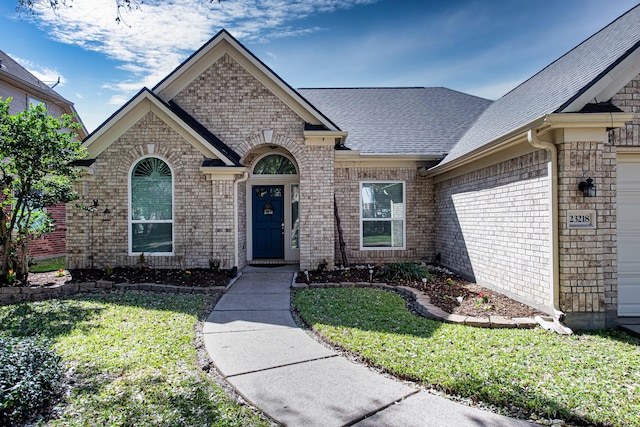 view of front facade featuring a garage, a front yard, brick siding, and roof with shingles