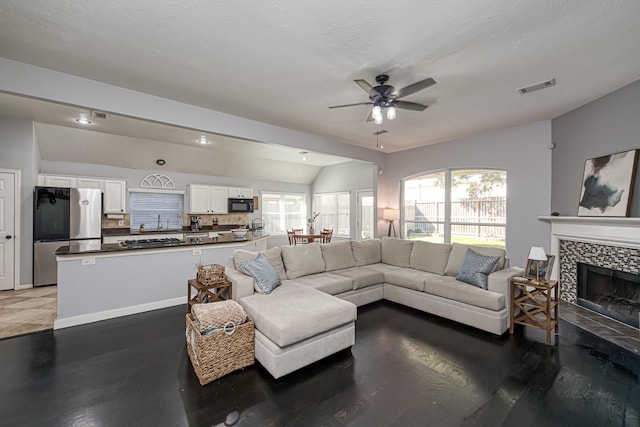 living room with visible vents, vaulted ceiling, ceiling fan, a tile fireplace, and baseboards