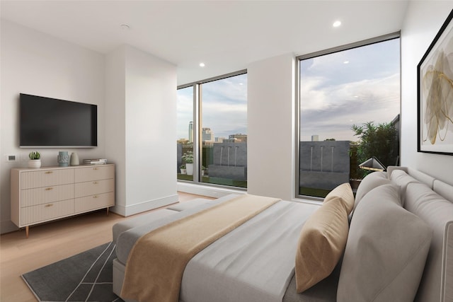 bedroom with a wall of windows, a view of city, recessed lighting, and light wood finished floors