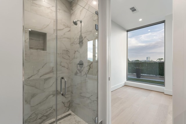 bathroom with wood finished floors, baseboards, visible vents, a marble finish shower, and expansive windows