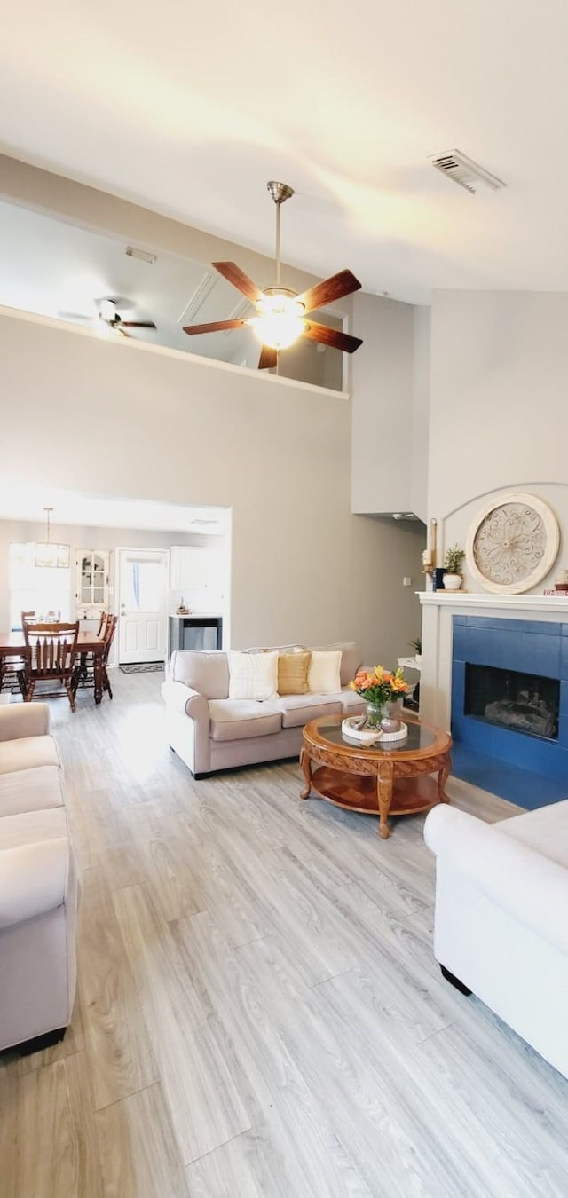 living room with a fireplace, visible vents, a ceiling fan, and wood finished floors