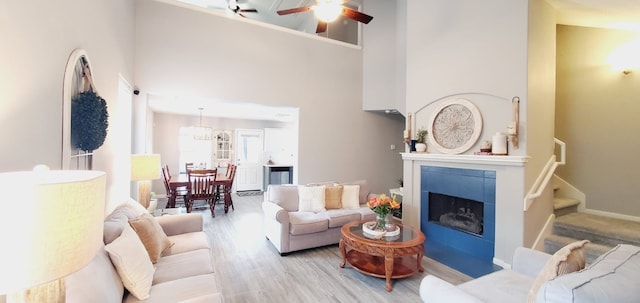 living room with a fireplace, stairway, a high ceiling, a ceiling fan, and wood finished floors