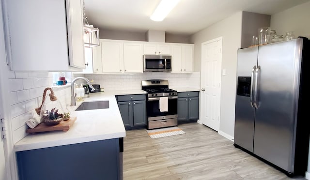 kitchen with light wood finished floors, tasteful backsplash, appliances with stainless steel finishes, light countertops, and a sink