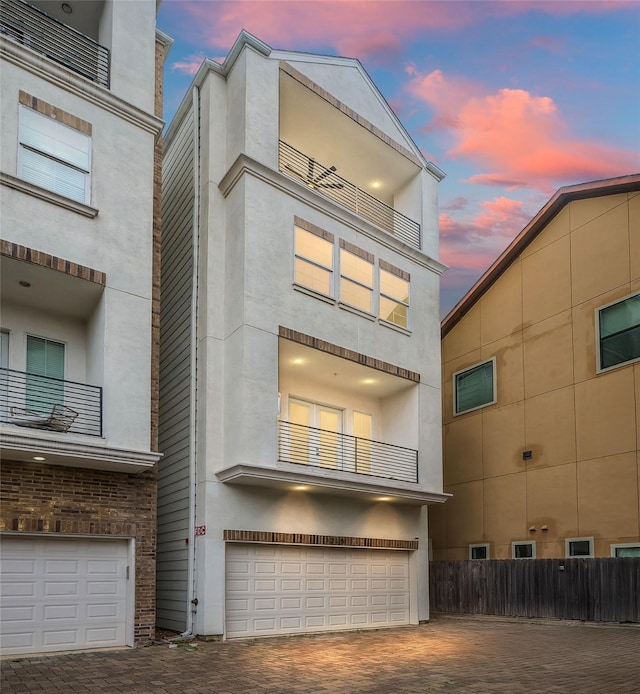 back of house at dusk featuring a garage, decorative driveway, and stucco siding