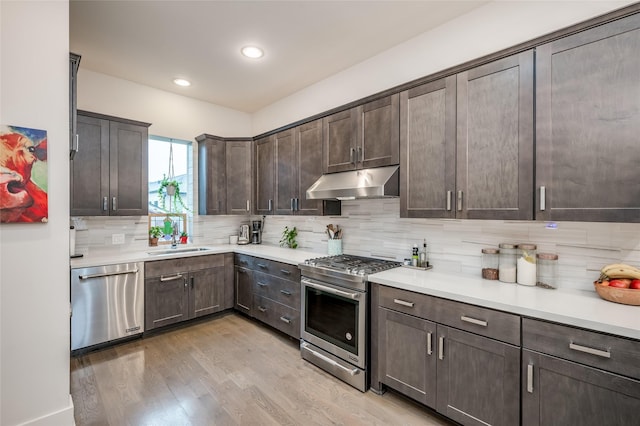 kitchen featuring dark brown cabinetry, under cabinet range hood, a sink, appliances with stainless steel finishes, and light wood-type flooring