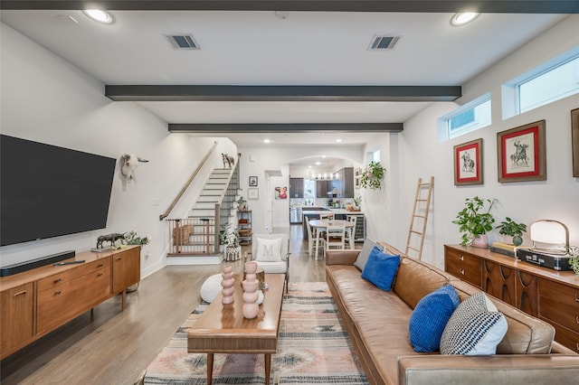 living area featuring visible vents, arched walkways, stairway, wood finished floors, and beam ceiling