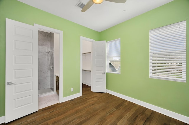 unfurnished bedroom with baseboards, visible vents, wood finished floors, a walk in closet, and a closet