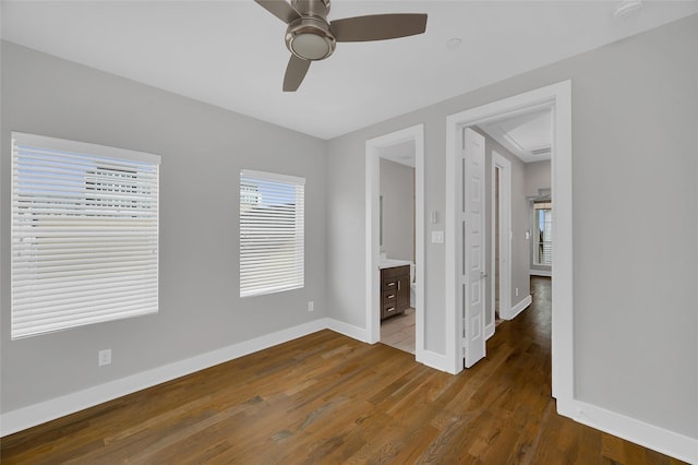 unfurnished bedroom with dark wood-style flooring, ensuite bath, a ceiling fan, and baseboards