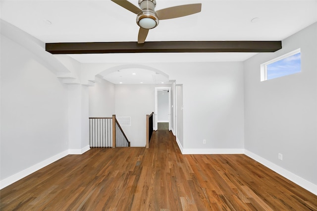 empty room featuring arched walkways, a ceiling fan, wood finished floors, beamed ceiling, and baseboards