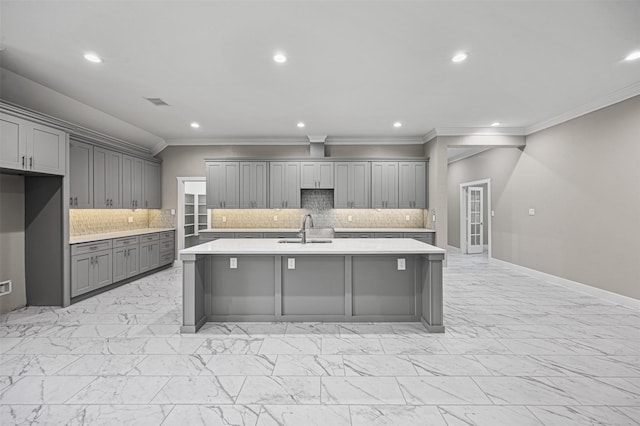 kitchen featuring marble finish floor, a kitchen island with sink, gray cabinets, light countertops, and a sink