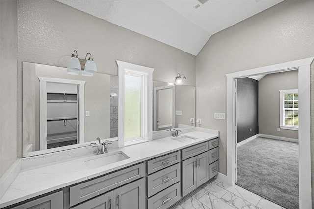 full bathroom featuring double vanity, marble finish floor, vaulted ceiling, and a sink